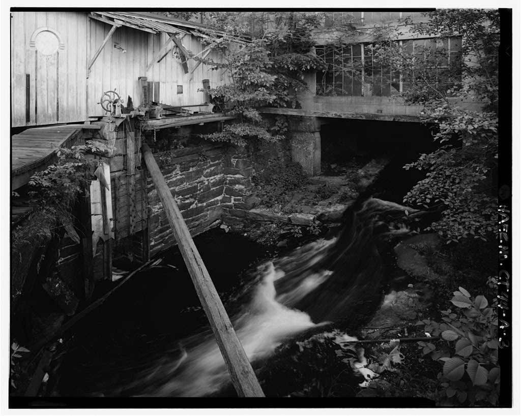 View west of headrace under warehouse; sluice gates at left center
